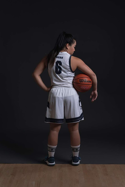 Photo of Jan holding up a 3 in a basketball uniform.